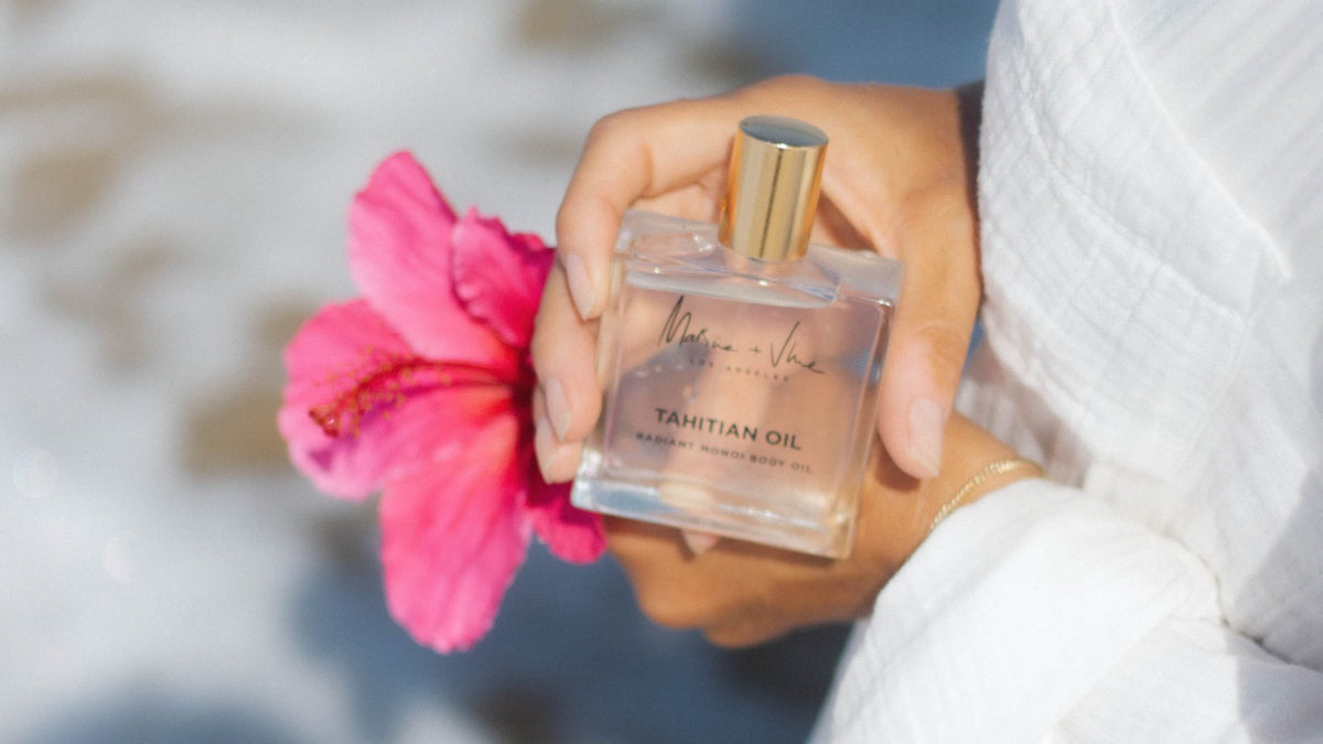 Evelyn Ginossi holding Marine + Vine Tahitian Oil with a pink hibiscus and white linen